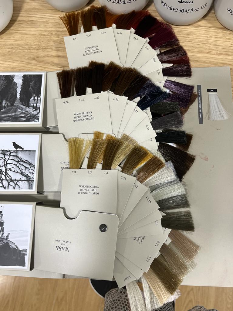 Muestra de colores de cabello con diferentes tonos cálidos de rubios, castaños y rojos, acompañada de productos de cuidado capilar en frascos. Ideal para salones de belleza y estilistas.