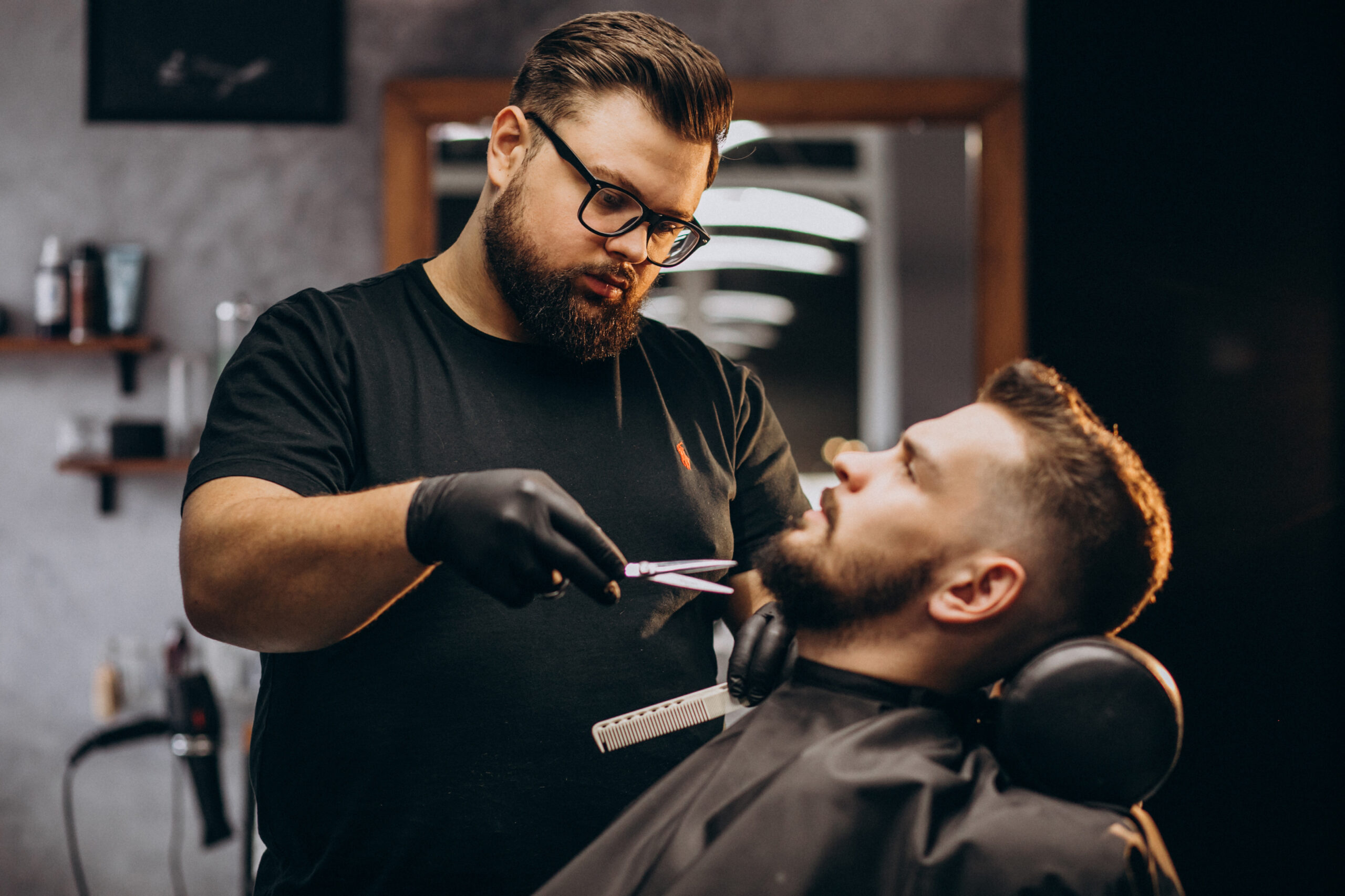Barbero cortando la barba de un cliente en una barbería moderna, con herramientas de corte y un ambiente profesional.